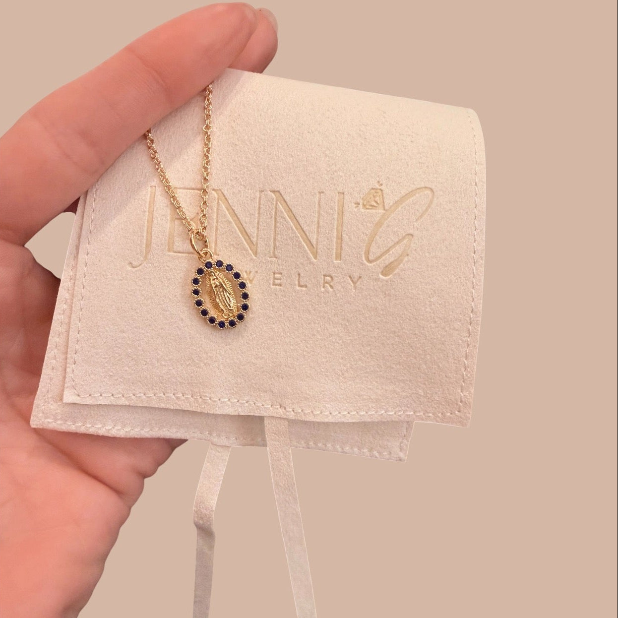 Gold necklace with a pendant on a Jenni Jewelry branded card held by a hand against a beige background